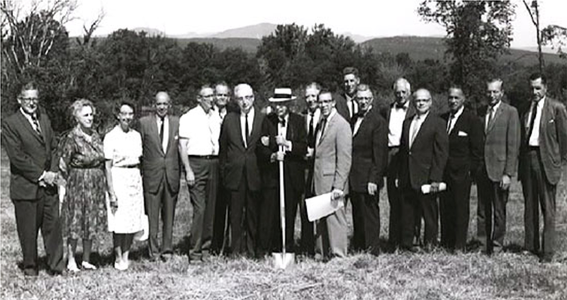 black and white photo of people dressed formally in 1960s, one with a shovel