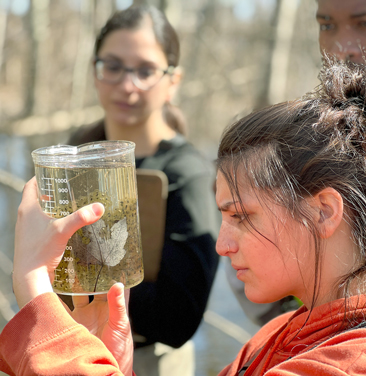 student outdoors examines jar of liquid with eggs